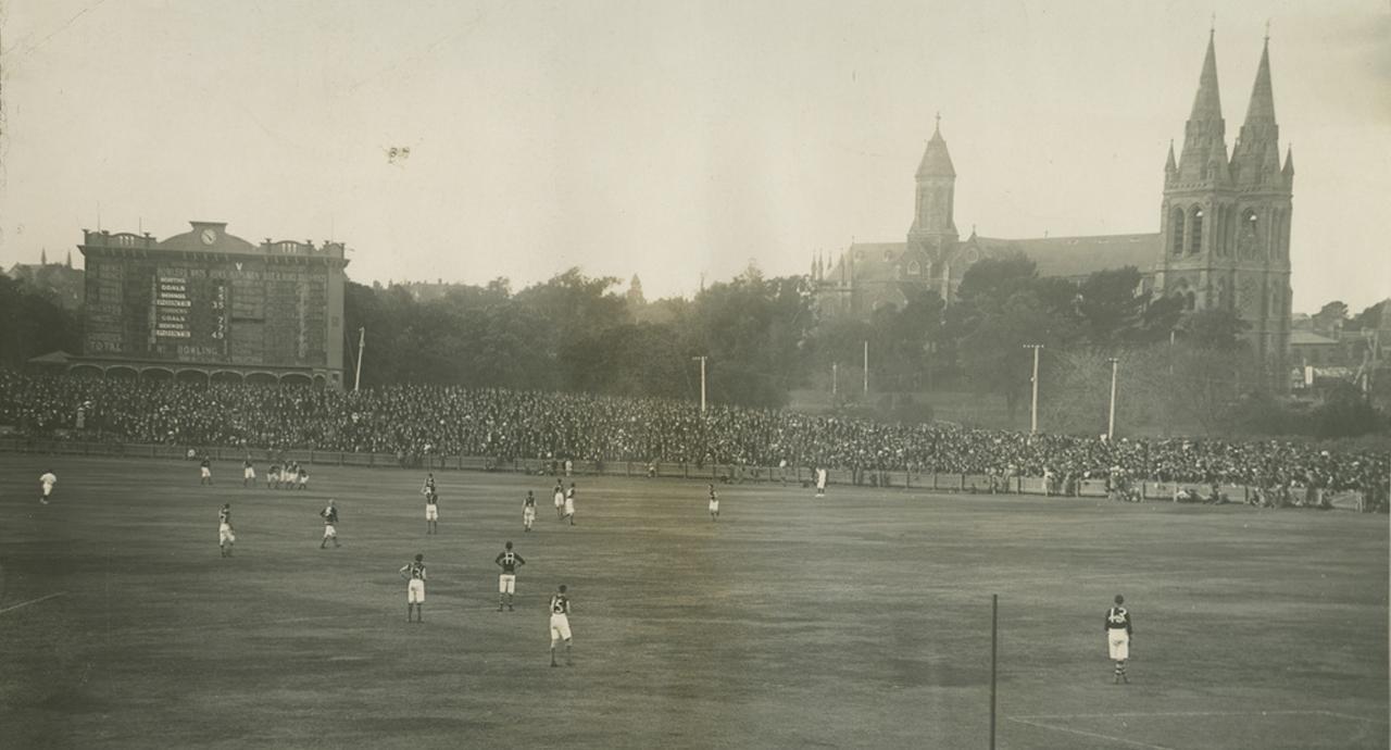 Photo of a football match at Adelaide Oval. Cathedral in the background.