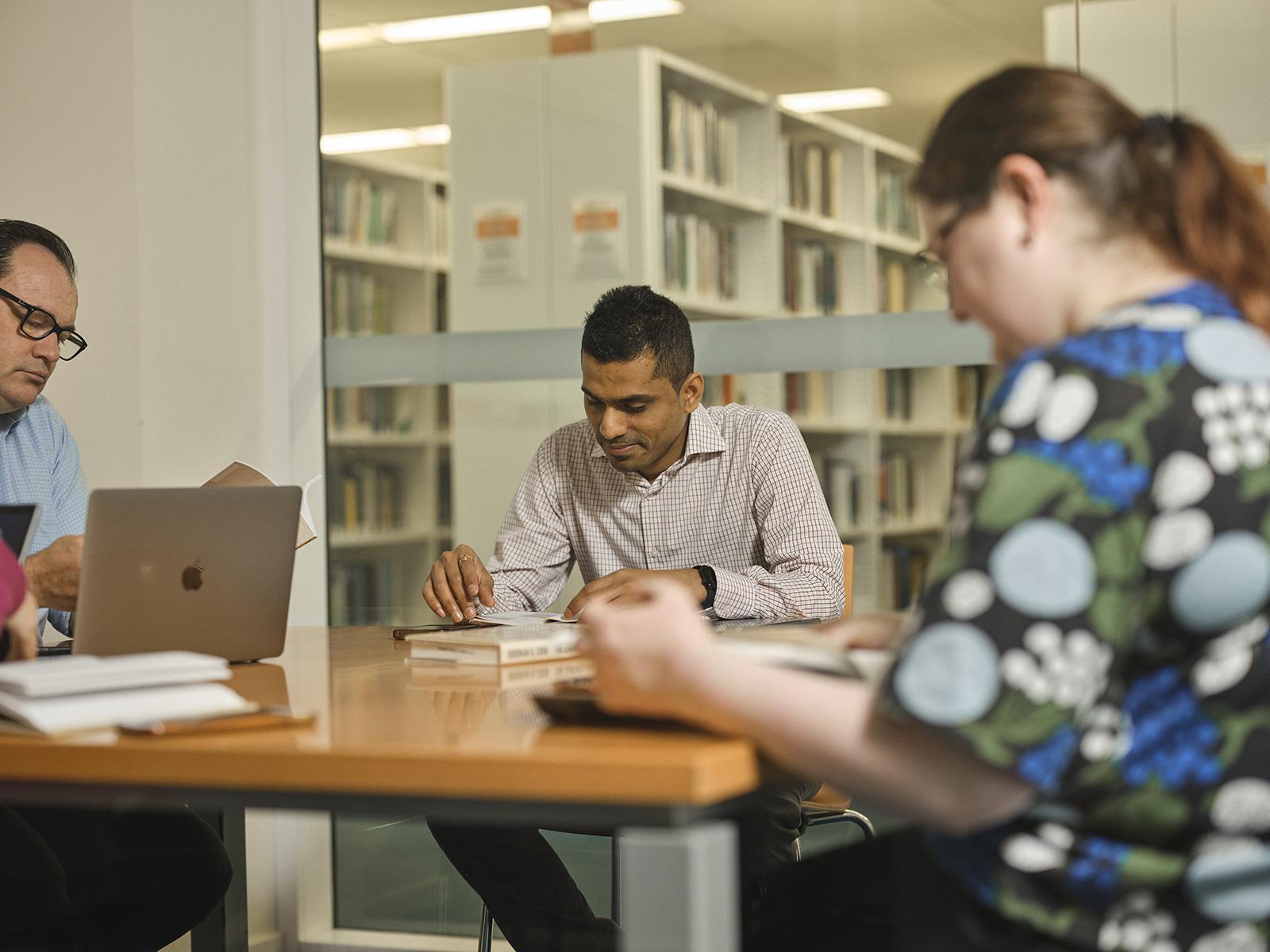 People sitting at a desk in a meeting room in a library.