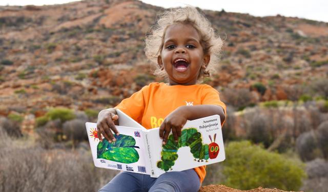 Young Indigenous child sitting on a rock reading a book