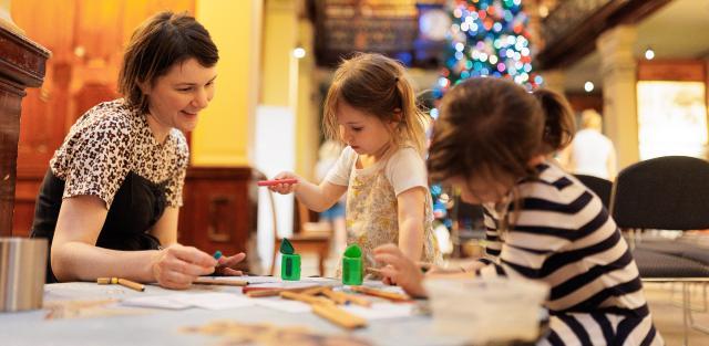 A lady sitting with two children at a small table doing craft.
