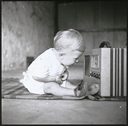 Baby leaning into a radio, 1938-1960, Raymond Heir Gordon. [SLSA: PRG1605/6/95]