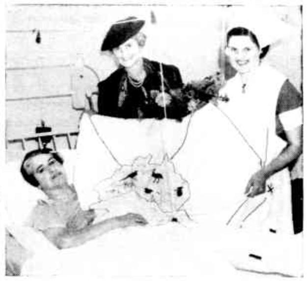 Doris Taylor lying in hospital bed showing map of Australia quilt to two women